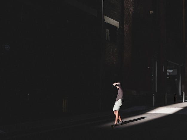 Vi standing in a dimly lit alleyway in Piltover, gazing into the distance with a conflicted expression. Her gauntlets are visible, and the scene is slightly blurred, suggesting a sense of introspection and isolation.