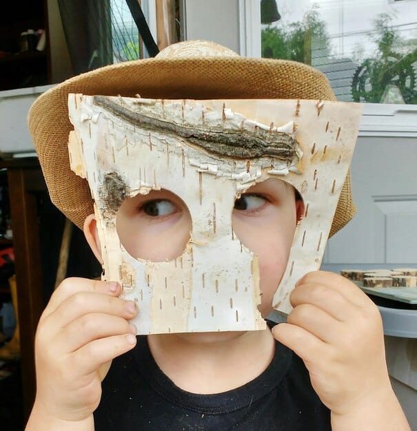 A close-up shot of a partially constructed Hoskel mask made primarily of layered cardboard. The cardboard pieces are visibly taped together, showing the rough initial shape. The image highlights the texture and construction process.